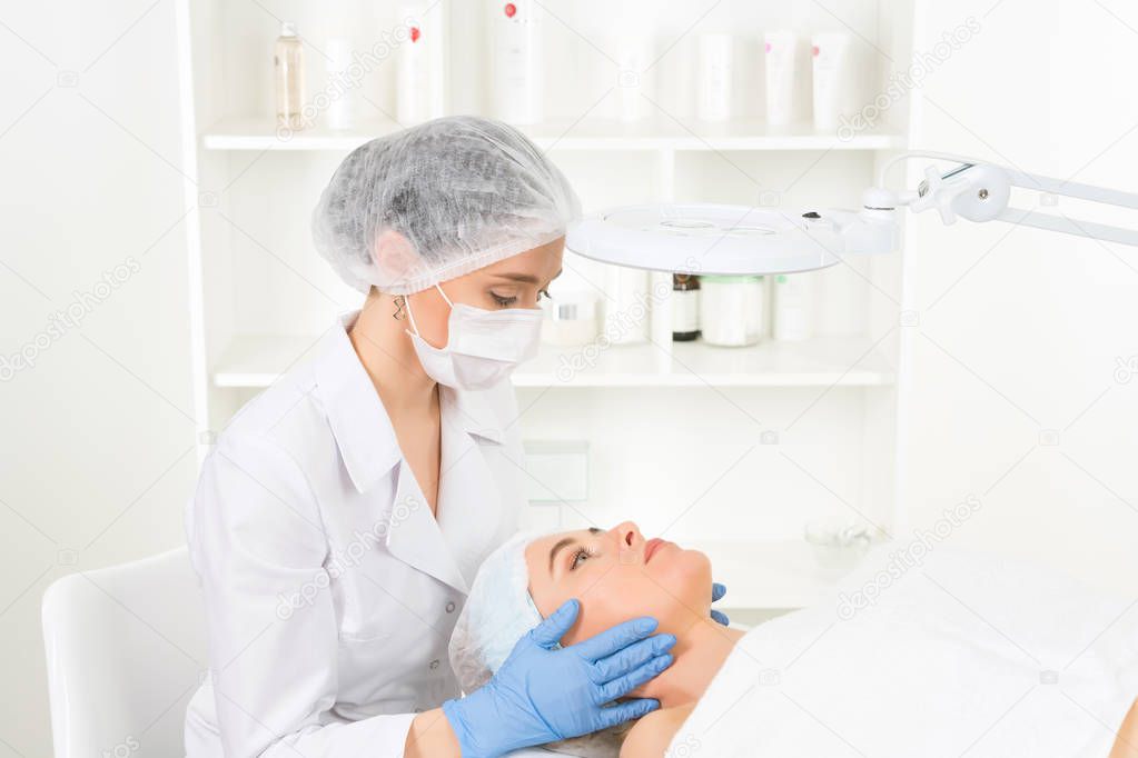 Female beautician doctor with patient in wellness center. Professional cosmetologist make procedure to beautiful girl in cosmetology cabinet or beauty parlor.