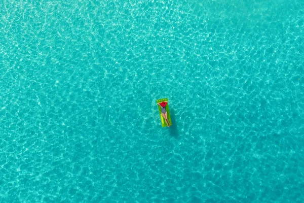 Aerial view of slim woman swimming on the swim mattress in the transparent turquoise sea in Seychelles. Summer seascape with girl, beautiful waves, colorful water. Top view from drone