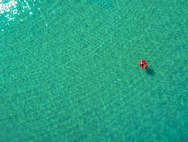 Вид с воздуха на стройную женщину, плавающую на пончике в прозрачном бирюзовом море на Сейшельских островах. Летний мыс с девушкой, красивые волны, красочная вода. Вид сверху с беспилотника
