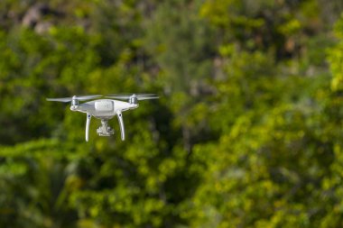 Uçan İHA, arka planda yeşil ağaçlar, İHA 'ya seçici odaklanma. 