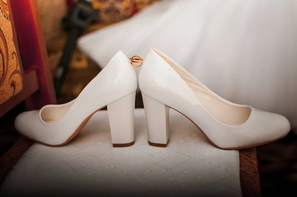 Dvojice zlatých svatebních prstenců mezi dvěma bílými botami — Stock fotografie
