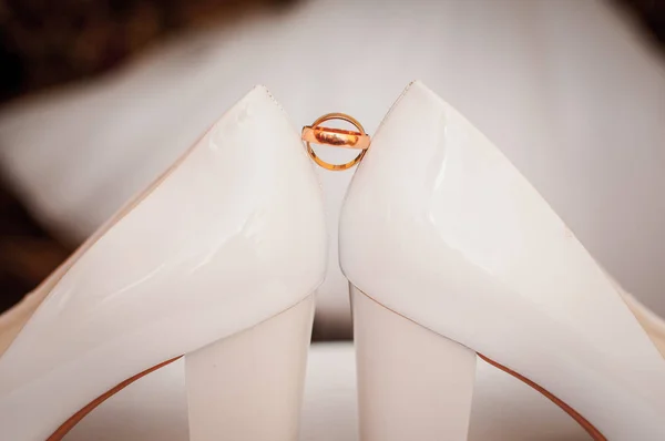Par de anillos de boda dorados entre un par de zapatos blancos — Foto de Stock