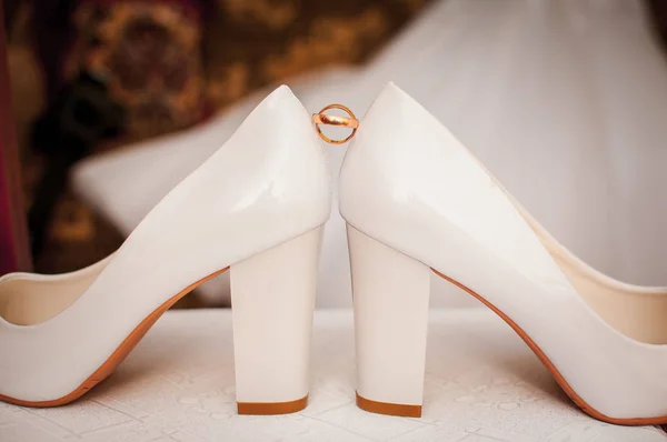 Pair of golden wedding rings between pair of a white shoes