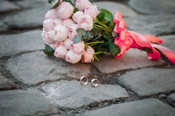 Anillos de boda de oro y ramo de flores rosa — Foto de Stock