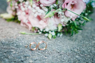 Yeşil çiçek buketi ve altın yüzük çifti ile Pembe asfalt yatıyor