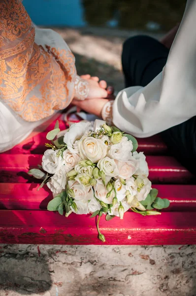 Manos de novia y novio con ramo de flores en el banco — Foto de Stock