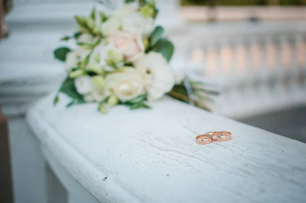 Три золотых обручальных кольца на белом мраморе с цветами — стоковое фото