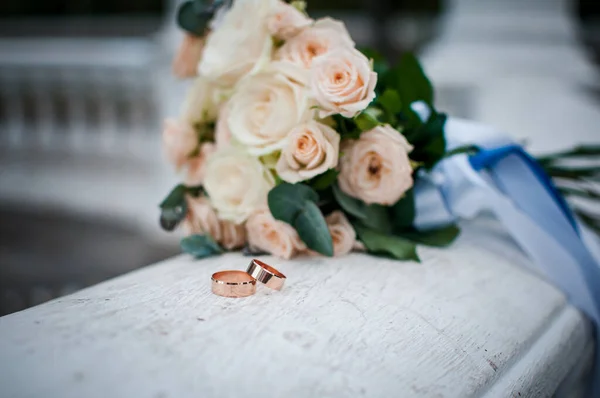 Pár zlatých svatebních prstenů na bílém mramoru s květinami — Stock fotografie
