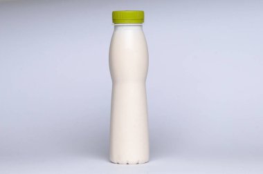 Beyaz fincanda yeşil bardak beyaz arka planda plastik süt şişesi.