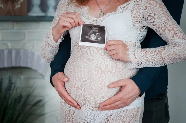 Uomo e donna tengono un'istantanea di un'ecografia su una pancia incinta — Foto Stock