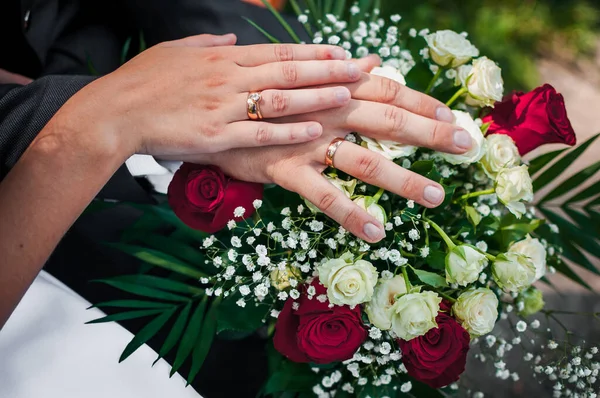 Обручки на руках молодят на весільний букет — стокове фото