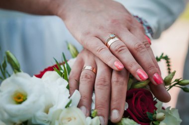 Düğün buketinde alyansları olan yeni evlilerin elleri