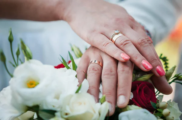 Friss házasok kezei jegygyűrűkkel esküvői csokorban — Stock Fotó