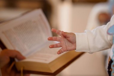 Bir bebeğin eli, vaftiz ya da vaftiz sırasında açık bir İncil 'e uzanır. İnancı, maneviyatı, umudu, yeni başlangıçları simgeler.