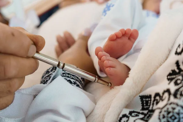 Yeni doğmuş bir bebeğe, yumuşak mavi ve beyaz tekstil içeren çelik bir mızrak kullanarak topuk iğnesi kan testi yapan bir sağlık hizmeti sağlayıcısının yakın çekimi.