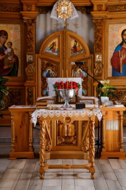 Gümüş bir kâsede kırmızı güllerle süslenmiş Ortodoks kilisesi sunağı, mumlar, ikonlar ve dini bir tören sunan ahşap bir masa.