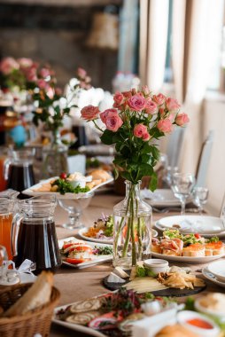 Çok güzel düzenlenmiş bir düğün masasında zarif pembe güller, iştah açıcı yemek tabakları, kristal cam eşyalar ve kırsal bir dekor sergileniyor.