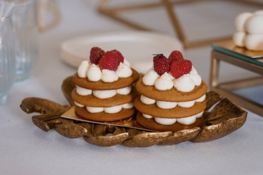 Taze kırmızı ahududu ile kaplanmış ve tüylü beyaz kremayla kaplı iki narin baharatlı kek ustalıkla altın yapraklı bir tepside sunuluyor.