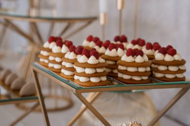 Krem şanti ve taze ahududu ile kaplı katmanlı badem badem kurabiyelerinin güzel bir düzenlemesi şık cam raflarda sergilenir, düğünler, tatlılar, lüks yemekler için mükemmeldir.
