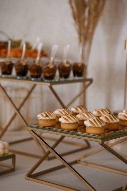 Güzel şekillendirilmiş bir tatlı masasında altın geometrik stantlarda sunulan minik tartlar ve çikolatalı mus fincanları, düğünler, partiler veya lüks yemek servisleri için mükemmeldir.