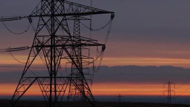 İngiltere 'nin Yorkshire kırsalında güneş doğarken siluetli elektrik direkleri ve elektrik hatları. Yüksek karşıtlık gökyüzü, durağan çerçeve, düz ufuk.