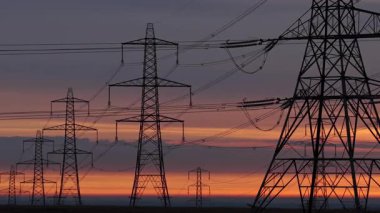 İngiltere 'nin Yorkshire kırsalında güneş doğarken siluetli elektrik direkleri ve elektrik hatları. Yüksek karşıtlık gökyüzü, durağan çerçeve, düz ufuk.