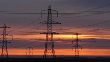 İngiltere 'nin Yorkshire kırsalında güneş doğarken siluetli elektrik direkleri ve elektrik hatları. Yüksek karşıtlık gökyüzü, durağan çerçeve, düz ufuk.