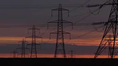 İngiltere 'nin Yorkshire kırsalında güneş doğarken siluetli elektrik direkleri ve elektrik hatları. Yüksek karşıtlık gökyüzü, durağan çerçeve, düz ufuk.