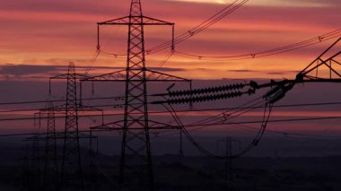 İngiltere 'nin Yorkshire kırsalında güneş doğarken siluetli elektrik direkleri ve elektrik hatları. Yüksek karşıtlık gökyüzü, durağan çerçeve, düz ufuk.