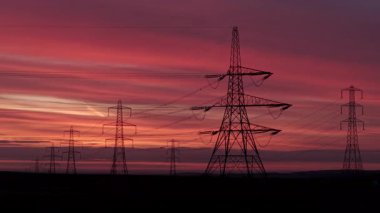 İngiltere 'nin Yorkshire kırsalında güneş doğarken siluetli elektrik direkleri ve elektrik hatları. Yüksek karşıtlık gökyüzü, durağan çerçeve, düz ufuk.