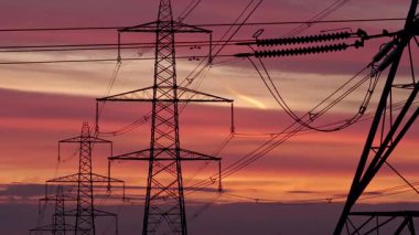 İngiltere 'nin Yorkshire kırsalında güneş doğarken siluetli elektrik direkleri ve elektrik hatları. Yüksek karşıtlık gökyüzü, durağan çerçeve, düz ufuk.