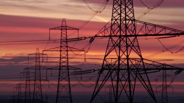 İngiltere 'nin Yorkshire kırsalında güneş doğarken siluetli elektrik direkleri ve elektrik hatları. Yüksek karşıtlık gökyüzü, durağan çerçeve, düz ufuk.