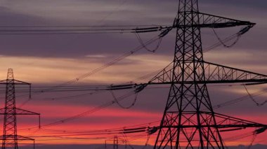 İngiltere 'nin Yorkshire kırsalında güneş doğarken siluetli elektrik direkleri ve elektrik hatları. Yüksek karşıtlık gökyüzü, durağan çerçeve, düz ufuk.