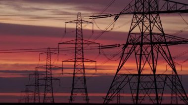 İngiltere 'nin Yorkshire kırsalında güneş doğarken siluetli elektrik direkleri ve elektrik hatları. Yüksek karşıtlık gökyüzü, durağan çerçeve, düz ufuk.