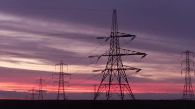 İngiltere 'nin Yorkshire kırsalında güneş doğarken siluetli elektrik direkleri ve elektrik hatları. Yüksek karşıtlık gökyüzü, durağan çerçeve, düz ufuk.