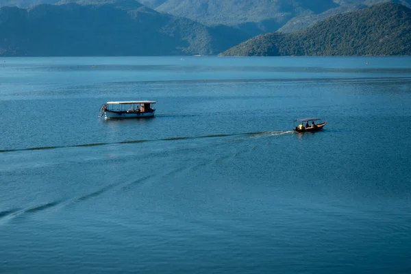 Sabahın erken saatlerinde gölün, ufkun ve arka planda dağların olduğu Skadar Gölü 'nün bir görüntüsü; turistleri taşıyan tekneler bir gezide süzülüyor. Karadağ, Skadar Gölü, 13 Ağustos 2025