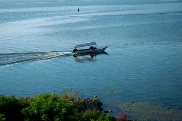 Sabahın erken saatlerinde gölün, ufkun ve arka planda dağların olduğu Skadar Gölü 'nün bir görüntüsü; turistleri taşıyan tekneler bir gezide süzülüyor. Karadağ, Skadar Gölü, 13 Ağustos 2025