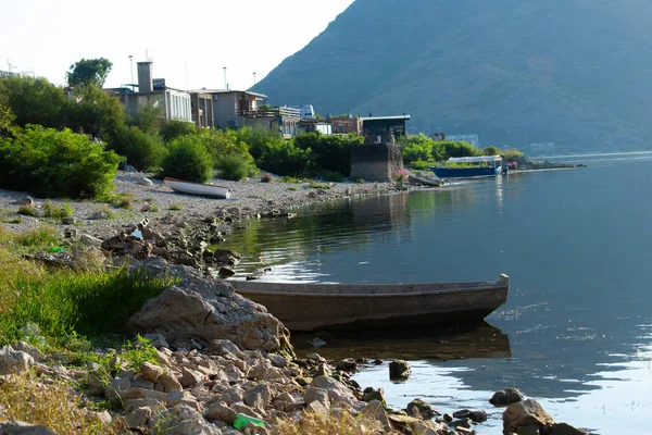 Bir resim, Skadar Gölü 'nün kayalık bir kıyısında arka planda balıkçılık yapan bir balıkçıyı gösteriyor. Karadağ, Skadar Gölü, 13 Ağustos 2025