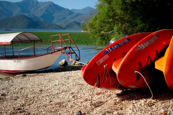 Skadar Gölü kıyısında bir balıkçı / turist teknesinin önünde renkli sörf tahtaları, arka planda dağlar. Karadağ, Skadar Gölü, 13 Ağustos 2025