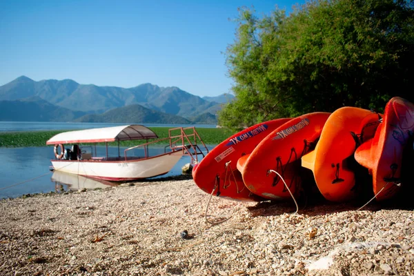 Skadar Gölü kıyısında bir balıkçı / turist teknesinin önünde renkli sörf tahtaları, arka planda dağlar. Karadağ, Skadar Gölü, 13 Ağustos 2025