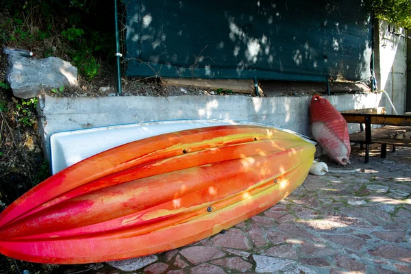 Beyaz beton bir duvarın yanında plastik kano tamir ediliyor.