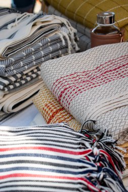 Görüntü, bir el sanatları festivalinde sergilenen Türk peshtemal havlusunu gösteriyor. Geleneksel tekstil işçiliği, parlak renkleri ve piyasa tarzı atmosferi olan bir aile şirketini vurguluyor.