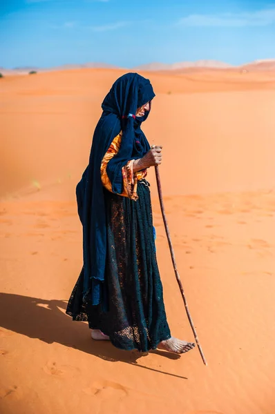 old  berber woman walking alone on a sand dune in Merzouga, Morocco