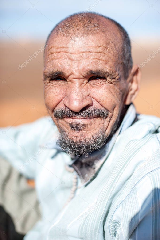 Portrait of old man who is resting on a dune erg chebbi at Merzouga, Morocco