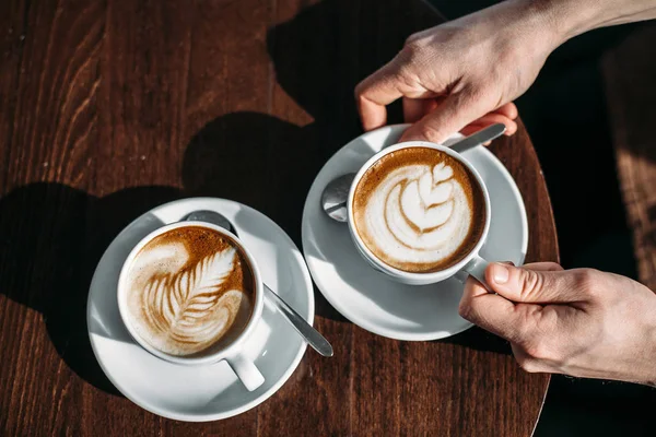 İki fincan cappuccino latte art adam elinde ahşap masa Tarih ile.