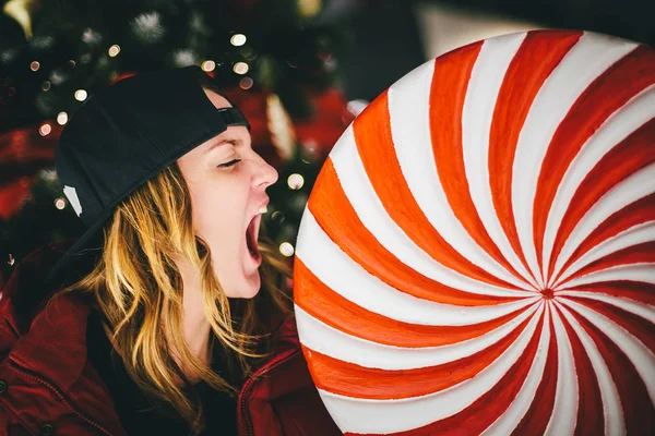 Noel ağacı ile dev lolipop arka plan üzerinde ısırma şık şapkası kırmızı ceketli trendy sevimli kız