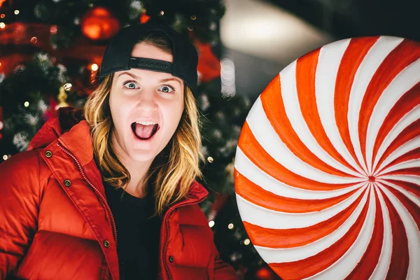 Arka plan üzerinde Noel ağacı ile dev lolipop ile şık şapkası kırmızı ceketli trendy sevimli kız