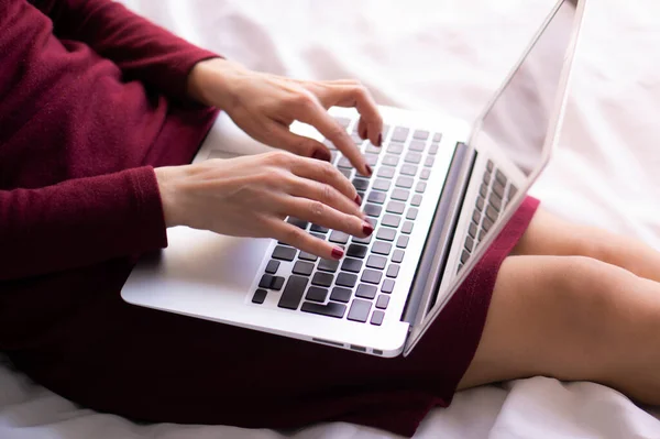 Genç bir kadın dizlerinin üstünde dizlerinin üstünde yatak odasındaki yatakta çalışıyor. Evde çalışıyorum..