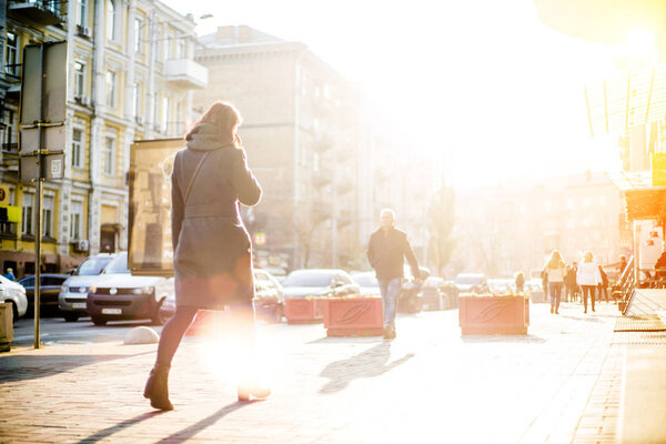 People with unrecognizable faces are walking through the streets fully shined by  evening warm