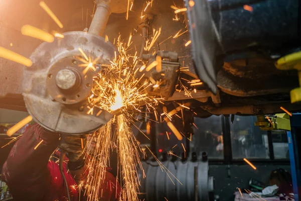 Young caucasian man in red work clothing repairing car with angle cutter. Many sparks on background.